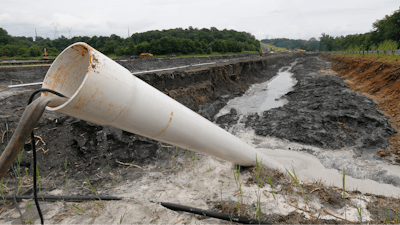 In this June 26, 2015 file photo a drain pipe sticks out of a coal ash retention pond at the Dominion Power's Possum Point Power Station in Dumfries, Va. A new report released Friday, Dec. 1, 2017, from Dominion Energy says it would be cheaper and quicker to close and cover coal ash ponds than to recycle the waste or move it to landfills.
