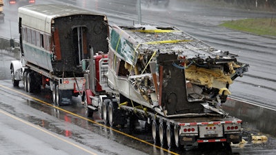 Two damaged train cars sit on flatbed trailers after being taken from the scene of an Amtrak train crash onto Interstate 5 a day earlier Tuesday, Dec. 19, 2017, in DuPont, Wash. Federal investigators say they don't yet know why the Amtrak train was traveling 50 mph over the speed limit when it derailed Monday south of Seattle.