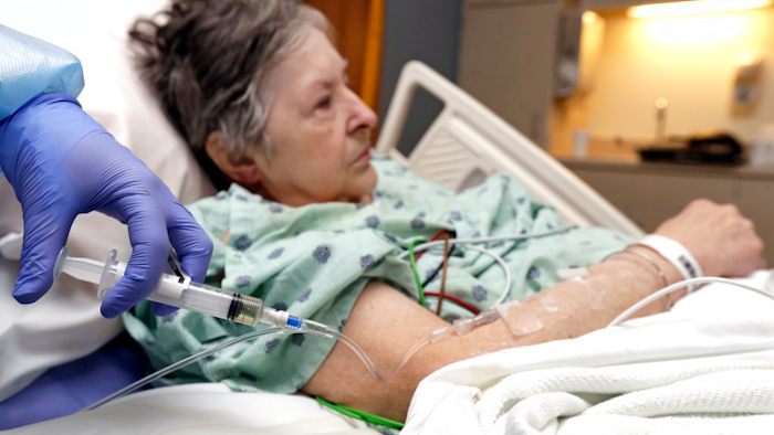 In this Monday, Jan. 8, 2018, photo, a nurse administers an I.V. push of antibiotics to Alice McDonald at ProMedica Toledo Hospital in Toledo, Ohio. A nasty flu season is hitting U.S. hospitals already scrambling to maintain patient care amid severe shortages of crucial sterile fluids, particularly saline solution needed to administer I.V. medicines and rehydrate patients.