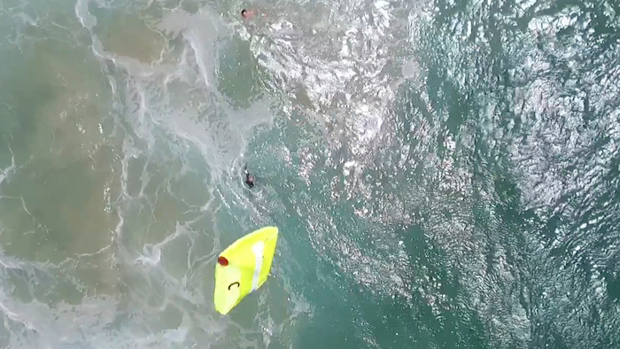 In this Thursday, Jan. 18, 2018 image made from a video provided by Westpac Little Ripper, a yellow flotation device is dropped from a flying drone toward two teenagers caught in a riptide in heavy seas off the Australian coast. A flying drone has dropped the flotation device to the pair in what officials describe as a world-first rescue. They were about a kilometer (0.6 mile) from lifeguards who were about to start training with the new drones, equipped with a camera, rescue gear and six rotors.
