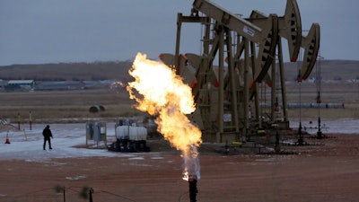 In this Oct. 22, 2015, file photo, workers tend to oil pump jacks behind a natural gas flare near Watford City, N.D. Fearing sanctions by the state, some North Dakota oil drillers have begun cutting output to control the amount of natural gas that's being burned off at well sites and wasted as a byproduct of crude production, industry and state officials say.