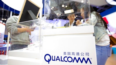 In this Thursday, April 27, 2017 file photo, visitors look at a display booth for Qualcomm at the Global Mobile Internet Conference (GMIC) in Beijing. The European Union is slapping a $1.23 billion fine on U.S. chipmaker Qualcomm for abusing its market dominance in the lucrative sector of vital components in smartphones and tablets.