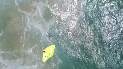 In this Thursday, Jan. 18, 2018 image made from a video provided by Westpac Little Ripper, a yellow flotation device is dropped from a flying drone toward two teenagers caught in a riptide in heavy seas off the Australian coast. A flying drone has dropped the flotation device to the pair in what officials describe as a world-first rescue. They were about a kilometer (0.6 mile) from lifeguards who were about to start training with the new drones, equipped with a camera, rescue gear and six rotors.
