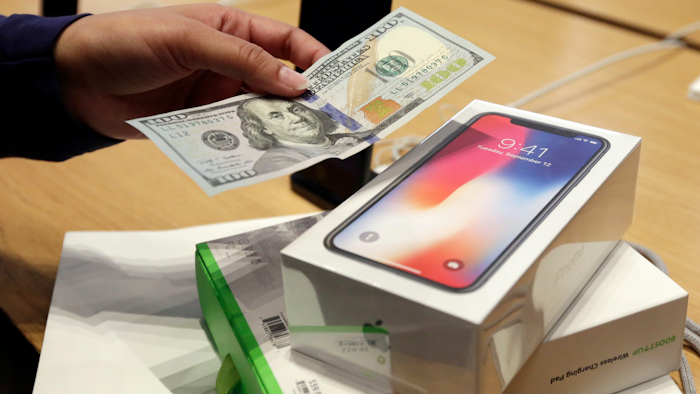 In this Friday, Nov. 3, 2017, file photo, a customer hands over cash as she pays for an iPhone X at the Apple Store on New York's Fifth Avenue. Apple is facing some thorny questions about its best-selling product, with conspiracy theories swirling around its secret slowdown of older iPhones and a cloud of uncertainty hanging over its big bet on the high-priced iPhone X.