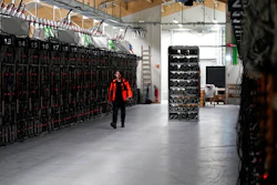 In this photo taken on Jan. 17, 2018, a worker walks along a row of computer rigs that run around the clock 'mining' bitcoin inside the Genesis Mining cryptocurrency mine in Keflavik, Iceland. Hand in hand with the rise of bitcoin is a soaring cost of “mining' the cryptocurrency. The energy demand has developed because of the soaring cost of producing the cryptocurrency, which requires computers solving math formulas to mine the 4.2 million coins still available.