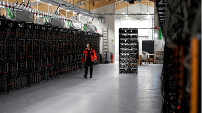In this photo taken on Jan. 17, 2018, a worker walks along a row of computer rigs that run around the clock 'mining' bitcoin inside the Genesis Mining cryptocurrency mine in Keflavik, Iceland. Hand in hand with the rise of bitcoin is a soaring cost of “mining' the cryptocurrency. The energy demand has developed because of the soaring cost of producing the cryptocurrency, which requires computers solving math formulas to mine the 4.2 million coins still available.