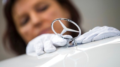 In this Jan. 24, 2018 file photo a woman fixes a Daimler Logo on a car at the Daimler AG company in Sindelfingen, Germany. Daimler AG says Thursday, Thursday, Feb. 1, 2018 its net profit rose 24 percent to a record 10.9 billion euros ($13.5 billion) last year, helped by strong sales of its Mercedes-Benz SUVs and new E-Class luxury sedan.