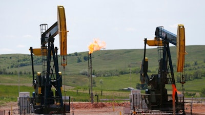 In this June 12, 2014 file photo, oil pumps and natural gas burn off in Watford City, N.D. The Interior Department says it is replacing an Obama-era regulation aimed at restricting harmful methane emissions from oil and gas production on federal lands. A rule being published in the Federal Register this week will replace the 2016 rule with requirements similar to those that were in force before the Obama administration changed the regulation.