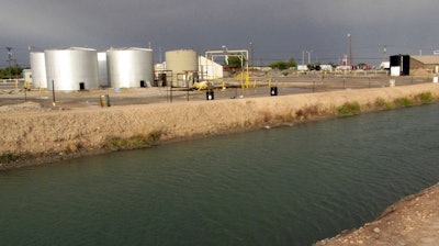 In this Oct. 28, 2009, file photo, empty water tanks sit at the edge of a brine well operation, shown at right of tanks, as a major irrigation canal flows by in Carlsbad, N.M. Experts are painting a dire picture for lawmakers about the impending collapse of a giant cavern that has formed under a highway interchange that serves as a gateway to southern New Mexico's oilfields and two national parks.
