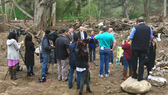 In this photo provided by G.F.Bunting survivor and co-plaintiff Lalo Barajas, center, whose partner Peter Fleurat was killed during devastating debris flows in January at their home, speaks at the site in Montecito, Calif, Thursday, March 29, 2018. Attorneys from left, Joseph Liebman, Geoff Spreter, Peter Bezerk, and Alex Robertson, right, announced the filing of a wrongful-death lawsuit by Barajas and Fleurat's siblings claiming Southern California Edison transformers ignited California's largest-ever wildfire in December. The suit says the blaze could have been prevented and the debris flows wouldn't have happened as a result.