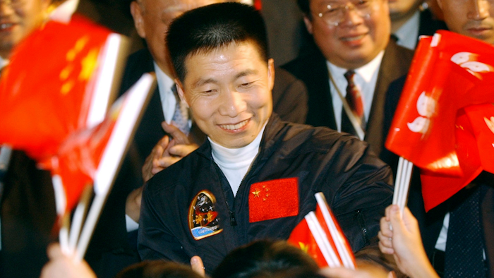 In this Oct. 31, 2003, file photo, school children wave Chinese and Hong Kong flags as they welcome China's first astronaut Yang Liwei, center, to Hong Kong's Government House for an official reception hosted by Hong Kong's Chief Executive Tung Chee-hwa, shortly after arriving for a five-day visit to the territory. China says it plans to begin recruiting civilian astronauts for its military-backed space program and increase the number of crewed missions to around two a year. Yang told reporters Saturday, March 3, 2018, new astronauts will include maintenance engineers and payload specialists as well as pilots.
