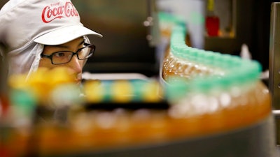 In this Nov. 17, 2016, file photo, a worker watches a product line at Coca-Cola Ebina plant in Ebina, Kanagawa Prefecture, near Tokyo. Coca-Cola may be getting into the booze business again by developing a bubbly alcoholic drink in Japan. The soda maker, best known for Coke, Sprite and Fanta, says it’s experimenting with a canned beverage that would be a mix of sparkling water and an alcoholic Japanese drink.