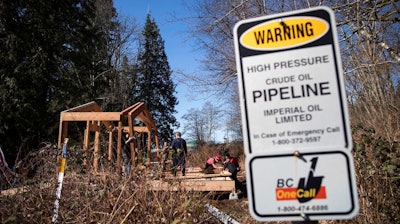A sign warns of an underground pipeline as people construct a 'watch house' near a gate leading to Kinder Morgan's property during a protest against the company's Trans Mountain pipeline expansion in Burnaby, British Columbia, Saturday, March 10, 2018.