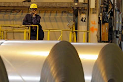 In this Feb. 15, 2013, file photo, an employee looks on from behind coils of steel as acting Secretary of Labor Seth Harris speaks to workers after a tour of ArcelorMittal Steel's hot dip galvanizing line in Cuyahoga Heights, Ohio. President Donald Trump’s tariffs are expected to raise prices for steel and aluminum in this country. That will help domestic producers and could create several hundred new steelworker jobs.