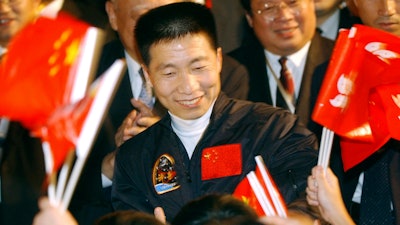 In this Oct. 31, 2003, file photo, school children wave Chinese and Hong Kong flags as they welcome China's first astronaut Yang Liwei, center, to Hong Kong's Government House for an official reception hosted by Hong Kong's Chief Executive Tung Chee-hwa, shortly after arriving for a five-day visit to the territory. China says it plans to begin recruiting civilian astronauts for its military-backed space program and increase the number of crewed missions to around two a year. Yang told reporters Saturday, March 3, 2018, new astronauts will include maintenance engineers and payload specialists as well as pilots.