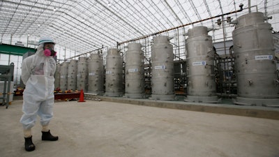 In this Nov. 12, 2014, file photo, a Tokyo Electric Power Co. (TEPCO) official wearing a radioactive protective gear stands in front of Advanced Liquid Processing Systems during a press tour at the Fukushima Dai-ichi nuclear power plant in Okuma, Fukushima Prefecture, northeastern Japan. A government-commissioned group of experts concluded Wednesday, March 7, 2018 that a costly underground ice wall is only partially effective in reducing the ever-growing amount of contaminated water at the destroyed Fukushima nuclear plant, and that other measures are needed as well.