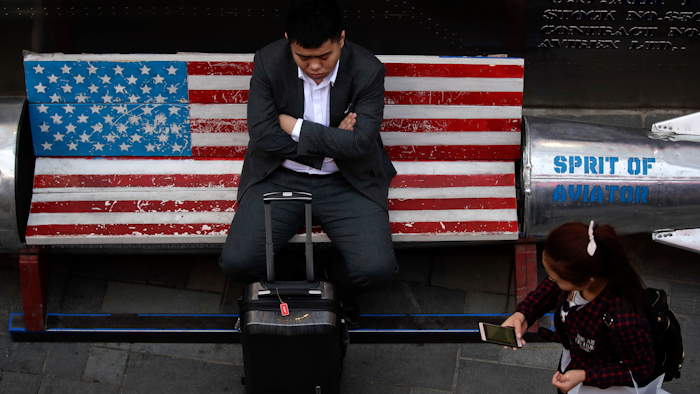 A woman walks by a man sitting outside an American apparel store at a shopping mall in Beijing, Tuesday, April 10, 2018. China's President Xi Jinping promised to cut auto import taxes, open China's markets further and improve conditions for foreign companies in a speech Tuesday that called for international cooperation against a backdrop of a spiraling dispute with Washington over trade and technology.
