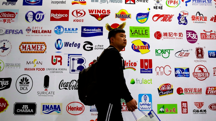 In this April 12, 2018, photo, a man walks by a billboard displaying a Chinese company developed packaging machinery for local and foreign food and beverage companies at the International soybean exhibition in Shanghai. Chinese soybean farmers, importers and processers say they are unconcerned about potential Chinese tariffs on American soybeans in an escalating dispute with the administration of President Donald Trump over trade and technology.