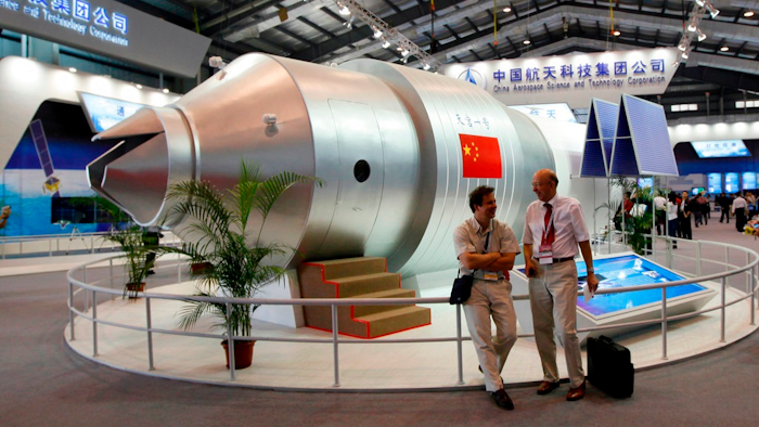 In this Nov. 16, 2010 file photo, visitors sit beside a model of China's Tiangong-1 space station at the 8th China International Aviation and Aerospace Exhibition in Zhuhai in southern China's Guangdong Province. China’s defunct Tiangong 1 space station is expected to re-enter Earth’s atmosphere within the next day. The European Space Agency forecast Sunday April 1, 2018 the station will re-enter sometime between Sunday night and early Monday morning GMT.
