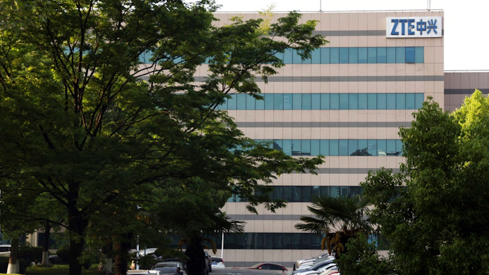 In this April 17, 2018, photo, a woman walks through the parking lot of a building hosting ZTE subsidiaries in Nanjing in eastern China's Jiangsu province. Chinese tech company ZTE said Friday, April 20, 2018, that it won't accept an 'unfair' U.S. penalty in a case involving exports of telecoms equipment to North Korea and Iran and is seeking a solution through legal channels.
