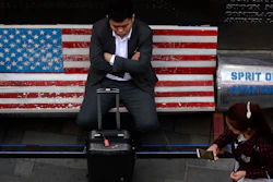 A woman walks by a man sitting outside an American apparel store at a shopping mall in Beijing, Tuesday, April 10, 2018. China's President Xi Jinping promised to cut auto import taxes, open China's markets further and improve conditions for foreign companies in a speech Tuesday that called for international cooperation against a backdrop of a spiraling dispute with Washington over trade and technology.