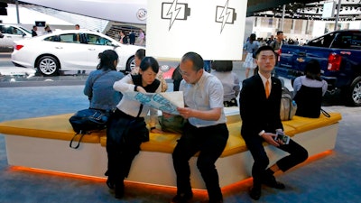 In this April 19, 2017, file photo, visitors to the stands of GM brands Chevrolet and Buick seat near a section promoting electric power during Auto Shanghai 2017 show at the National Exhibition and Convention Center in Shanghai, China. China has announced plans to allow full foreign ownership of automakers in five years, ending restrictions that have strained relations with Washington and other trading partners.