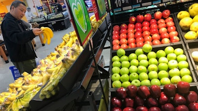 A man chooses bananas near imported apples from the United States at a supermarket in Beijing, Monday, April 2, 2018. China raised import duties on a $3 billion list of U.S. pork, fruit and other products Monday in an escalating tariff dispute with President Donald Trump that companies worry might depress global commerce.