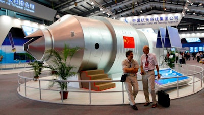 In this Nov. 16, 2010 file photo, visitors sit beside a model of China's Tiangong-1 space station at the 8th China International Aviation and Aerospace Exhibition in Zhuhai in southern China's Guangdong Province. China’s defunct Tiangong 1 space station is expected to re-enter Earth’s atmosphere within the next day. The European Space Agency forecast Sunday April 1, 2018 the station will re-enter sometime between Sunday night and early Monday morning GMT.