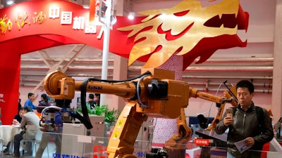 In this Oct. 21, 2016 file photo, visitors look at industrial robots displayed beneath the words that read 'Chinese Robots' during the World Robot Conference in Beijing. U.S. officials have a name for their frustration with Beijing’s technology ambitions: ‘Made in China 2025.’ President Donald Trump’s government says China’s plan to create global competitors in fields from information technology to electric cars to pharmaceuticals is an example of policies that prompted Trump’s threat to hike tariffs on $50 billion of Chinese goods. They say China’s tactics include improperly subsidizing local and pressuring foreign competitors to hand over technology.
