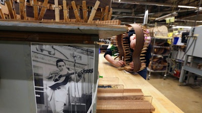 In this Friday, March 23, 2018 photo, a photo of Johnny Cash hangs near a luthier assembling the rosewood sides of a guitar at C. F. Martin and Co., in Nazareth, Pa. The cost and hassle of the new regulations on rosewood have caused some guitar makers to shift away from it. Martin stopped using it on most guitars produced in Mexico and the models made in the U.S. that cost less than $3,000.