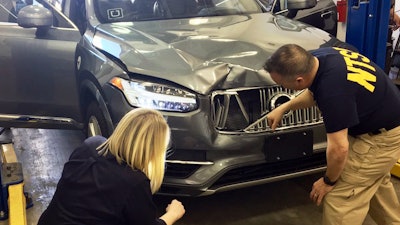 In this March 20, 2018, photo provided by the National Transportation Safety Board, investigators examine a driverless Uber SUV that fatally struck a woman in Tempe, Ariz. The fatality prompted Uber to suspend all road-testing of such autos in the Phoenix area, Pittsburgh, San Francisco and Toronto.