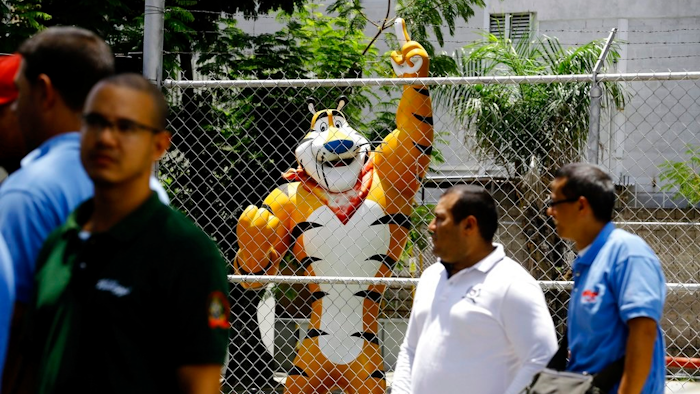 A statue of Kellogg's mascot, Tony the Tiger, stands behind the Kellogg's factory's fence, as workers gather outside in Maracay, Venezuela, Tuesday, May 15, 2018. Workers arriving Tuesday for the early shift were surprised to find a notice taped to an iron gate informing them that the company had been forced to shutter its operations.
