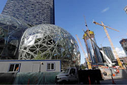 In this Wednesday, Oct. 11, 2017, file photo, large spheres take shape in front of an existing Amazon building, behind, as new construction continues across the street in Seattle. Amazon said Wednesday, May 2, 2018, it is pausing construction on a new high-rise building in Seattle while it awaits the outcome of a city proposal to tax worker hours. The Seattle City Council has been weighing a proposed 'head tax' on high-grossing businesses as a way to raise about $75 million a year for affordable housing and homelessness services.
