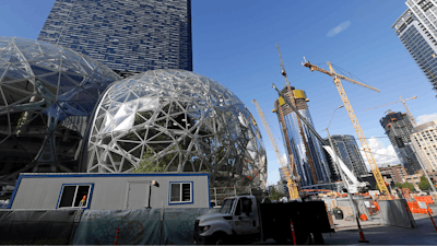 In this Wednesday, Oct. 11, 2017, file photo, large spheres take shape in front of an existing Amazon building, behind, as new construction continues across the street in Seattle. Amazon said Wednesday, May 2, 2018, it is pausing construction on a new high-rise building in Seattle while it awaits the outcome of a city proposal to tax worker hours. The Seattle City Council has been weighing a proposed 'head tax' on high-grossing businesses as a way to raise about $75 million a year for affordable housing and homelessness services.