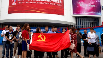 Visitors to the 21st China Beijing International High-tech Expo pose for photos with a Chinese flag in Beijing, China, Thursday, May 17, 2018. The Trump administration has threatened to impose tariffs on up to $150 billion in Chinese imports to punish Beijing over trade practices requiring American companies to hand over technology in exchange for access to the Chinese market. China has counterpunched by targeting $50 billion in U.S. products.