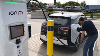 In this Friday, May 11, 2018 photo a man charges his BMW electric vehicle at the rest stop Brohltal Ost at the A61 motorway in Niederzissen, Germany. Munich-based Ionity build a highway network of fast charging stations that will let drivers plug in, charge in minutes instead of hours, and speed off on their way, from Norway to southern Italy and Portugal to Poland