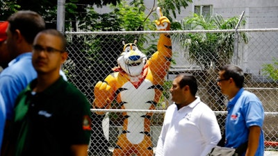 A statue of Kellogg's mascot, Tony the Tiger, stands behind the Kellogg's factory's fence, as workers gather outside in Maracay, Venezuela, Tuesday, May 15, 2018. Workers arriving Tuesday for the early shift were surprised to find a notice taped to an iron gate informing them that the company had been forced to shutter its operations.