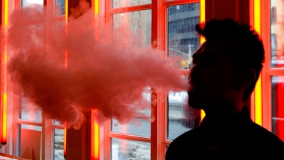 In this Feb. 20, 2014 file photo, a customer exhales vapor from an e-cigarette at a store in New York. In a large study of company wellness programs released on Wednesday, May 23, 2018, e-cigarettes worked no better than traditional stop-smoking tools, and the only thing that really helped was paying folks to kick the habit.