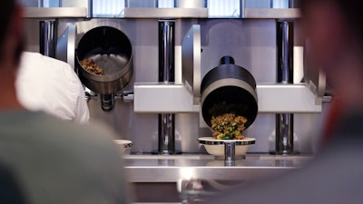 Customers wait as their automatically prepared food is dropped from a cooking pot into a bowl at Spyce, a restaurant which uses a robotic cooking process in Boston, Thursday, May 3, 2018. Robots can't yet bake a souffle or fold a burrito, but the new restaurant in Boston is employing what it calls a 'never-before-seen robotic kitchen' to cook up ingredients and spout them into a bowl.