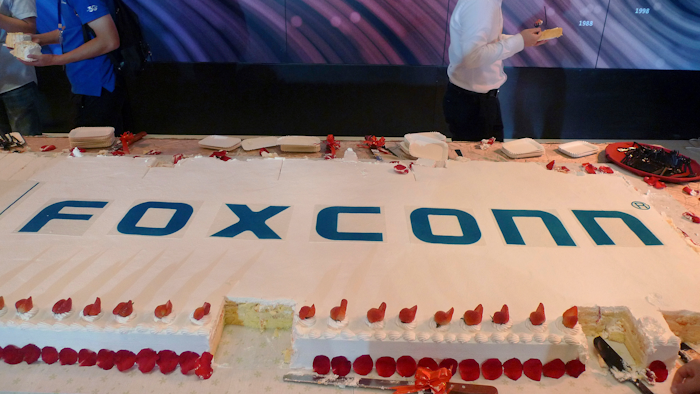 Workers walk past a giant cake to celebrate Taiwan-based contract manufacturing giant Foxconn's 30th anniversary of its first investment in Shenzhen, south China's Guangdong province Wednesday, June 6, 2018. The head of Taiwan's Foxconn, which assembles Apple iPhones and other tech products, says Washington's dispute with China is over technology rather than trade.