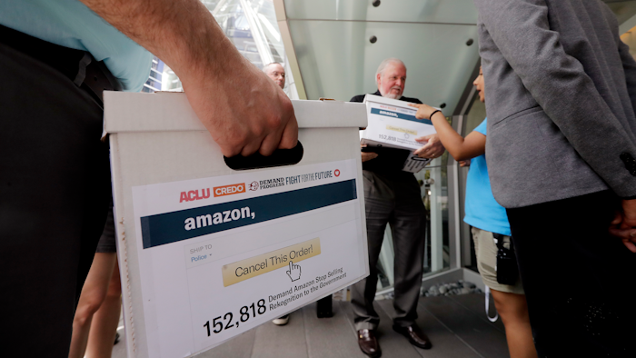 Faith leader the Rev. Paul Benz, center, and Shankar Narayan, legislative director of the ACLU of Washington, right, stand with others as they wait to deliver petitions at Amazon headquarters, Monday, June 18, 2018, in Seattle. Representatives of community-based organizations urged Amazon at a news conference to stop selling its face surveillance system, Rekognition, to the government. They later delivered the petitions to Amazon.