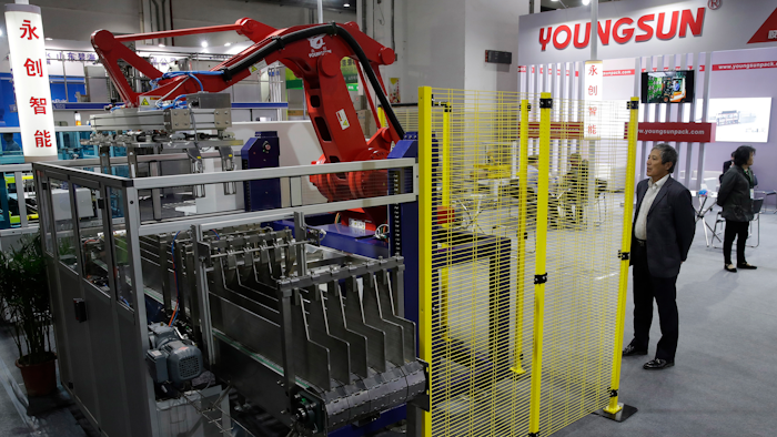 In this April 12, 2018, photo, a visitor watches a Chinese company displaying a Chinese-made industrial robot demonstration on processing soybean at the International soybean exhibition in Shanghai. China says it will narrow its trade surplus with the United States but rejects pressure to change technology development tactics seen as a path to prosperity and its rightful place as a global leader. Beijing highlighted the sensitivity of the issue with its threat to scrap deals aimed at settling a sprawling trade dispute with Washington if President Donald Trump's threatened tariff hike on $50 billion of Chinese technology goes ahead.