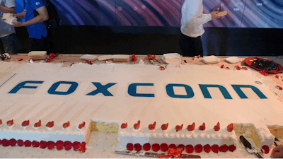 Workers walk past a giant cake to celebrate Taiwan-based contract manufacturing giant Foxconn's 30th anniversary of its first investment in Shenzhen, south China's Guangdong province Wednesday, June 6, 2018. The head of Taiwan's Foxconn, which assembles Apple iPhones and other tech products, says Washington's dispute with China is over technology rather than trade.