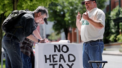 In this May 24, 2018, photo, paid signature gatherer John Ellard, right, gives thumbs-up as two men stop to sign petitions to put on the November ballot a referendum on Seattle's head tax, in Seattle. Seattle city leaders say they'll work to repeal the tax passed just last month on businesses such as Amazon and Starbucks designed to help pay for homeless services and affordable housing. Amazon and other businesses had sharply criticized the levy, and the online retail giant even temporarily halted construction planning on a new high-rise building near its Seattle headquarters in protest.