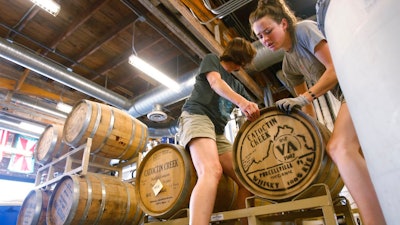 In this Wednesday, June 20, 2018, photo Becky Harris left, and Addie Rodgers move a barrel of whiskey in the Catoctin Creek Distillery in Purcellville, Va. Rye whiskey is aging in hundreds of barrels at Catoctin Creek Distillery, and based on market trends about one-fourth of the inventory could end up being consumed in Europe, a market the 9-year-old distilling company has cultivated at considerable cost.
