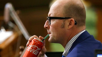 Assemblyman Matthew Harper, R-Huntington Beach, sips a Coke as Assembly members debate a ban on local soda taxes, Thursday, June 28, 2018, in Sacramento, Calif. Lawmakers passed a bill to ban local taxes on soda for the next 12 years and send it to the Gov. Jerry Brown. Harper did not cast on vote on the bill.