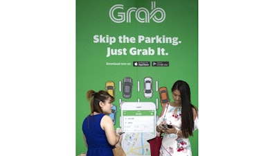 In this March 26, 2018, file photo, passengers wait for Grab car outside a shopping man in Kuala Lumpur, Malaysia. Japan's top automaker Toyota Motor Corp. is investing $1 billion in Grab, the leading ride-hailing company in Southeast Asia, the company said Wednesday, June 13, 2018.