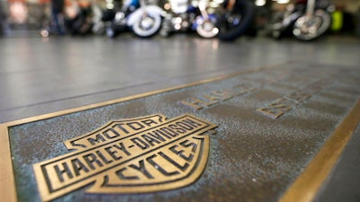 In this April 26, 2017, file photo, rows of motorcycles are behind a bronze plate with corporate information on the showroom floor at a Harley-Davidson dealership in Glenshaw, Pa. Harley-Davidson, facing rising costs from new tariffs, will begin shifting the production of motorcycles heading for Europe from the U.S. to factories overseas.