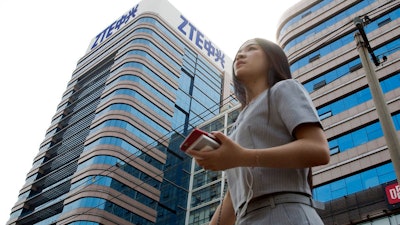 In this May 8, 2018, file photo, a woman passes by a ZTE building in Beijing, China. Chinese tech giant ZTE Corp.'s chairman promised no further compliance violations and apologized to customers in a letter Friday, June 8, 2018, for disruptions caused by its violation of U.S. export controls, a newspaper reported.