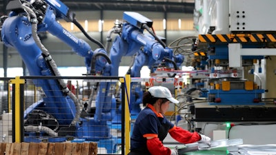 In this Tuesday, June 5, 2018 photo, a worker assembles air conditioner's components next to the robot arms at a factory in Suixi county in central China's Anhui province. China's politically sensitive trade surplus with the United States widened in May from a year earlier while its global trade gap shrank as imports accelerated. The latest reading on trade comes amid U.S. pressure on Beijing over its trade surplus and technology policy.